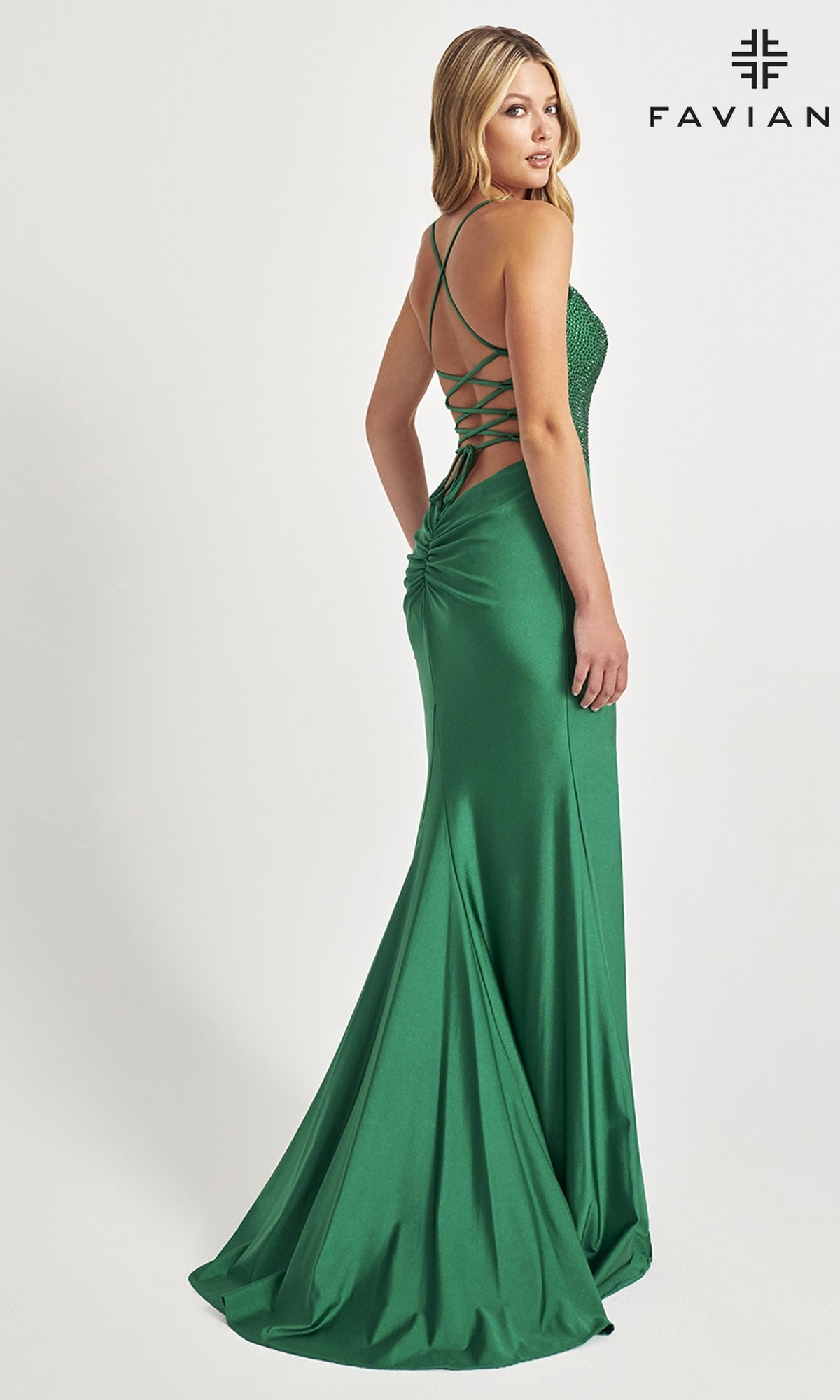 A woman wearing the Beaded-Corset-Bodice Faviana Long Prom Dress 11011 in fitted green with a lace-up open back stands against a plain white background.